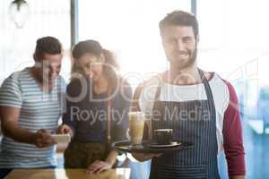 Smiling waiter holding coffee in tray at cafÃ?Â©