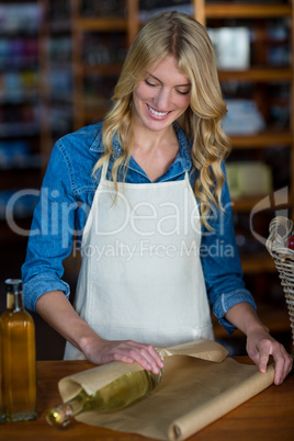 Smiling female staff wrapping olive oil bottle with brown paper