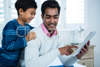 Father showing digital tablet to son on the bed