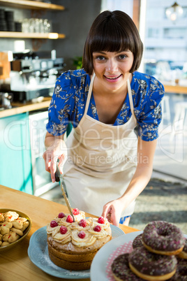 Smiling waitress cutting a cake in the coffee shop