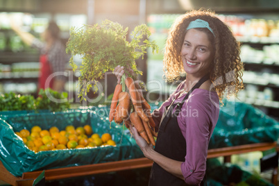 Smiling female staff holding bunch of carrots in organic section