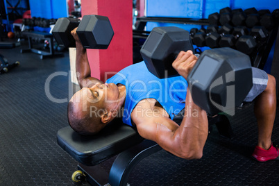 Male athlete exercising with dumbbells in gym