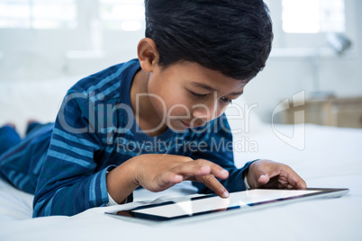 Boy using digital tablet while relaxing on bed