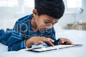 Boy using digital tablet while relaxing on bed