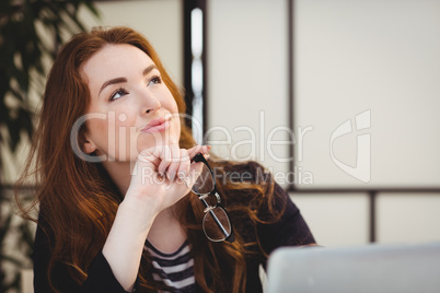 Thoughtful beautiful woman holding eyeglasses while looking up at creative office