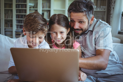 Father sitting on sofa with his children and using laptop in living room