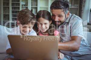 Father sitting on sofa with his children and using laptop in living room