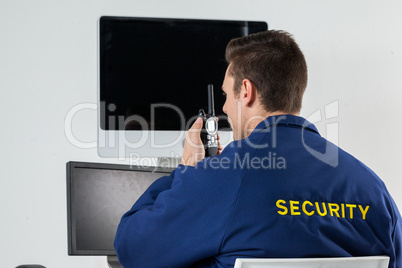 Security officer talking on walkie-talkie while looking at computer monitors
