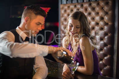 Waiter pouring a cocktail in woman glass at bar counter