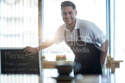 Smiling waiter writing on menu board in cafe