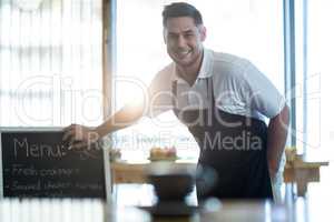 Smiling waiter writing on menu board in cafe