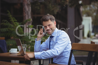 Handsome businessman talking on mobile phone while using laptop