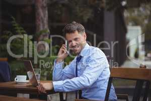 Handsome businessman talking on mobile phone while using laptop