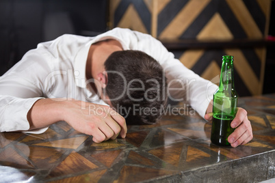 Drunk man lying on a counter with bottle of beer