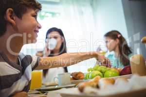 Boy picking up fruits from tray while having breakfast