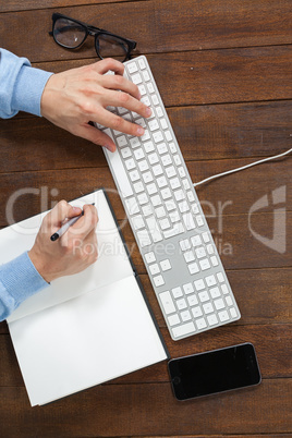 Man typing on keyboard and writing in diary