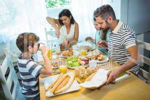 Woman cutting loaf of bread while family having breakfast