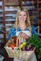 Smiling female staff holding basket of vegetables in organic section