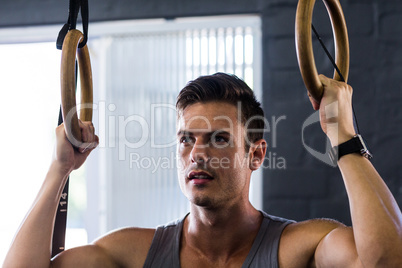 Close-up of young man using gymnastic rings in gym