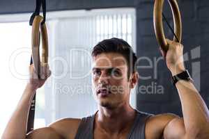 Close-up of young man using gymnastic rings in gym