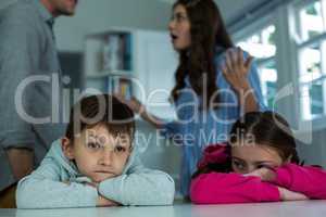 Upset children sitting while couple arguing with each other