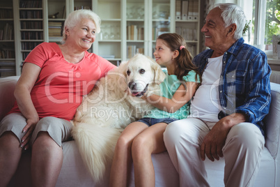 Grandparents and granddaughter sitting on sofa with pet dog