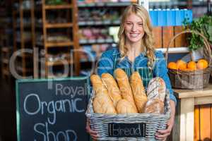 Smiling woman holding a basket of baguettes in organic shop