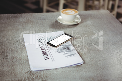 Mobile phone with newspaper and coffee cup on a table