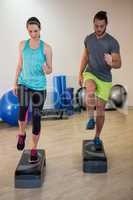Man and woman doing step aerobic exercise on stepper