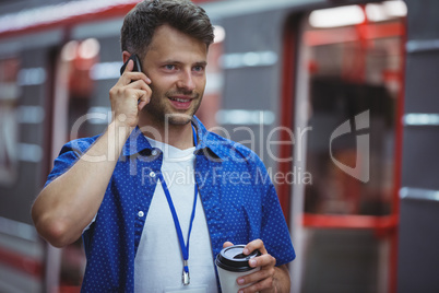 Handsome holding disposable cup while talking on mobile phone