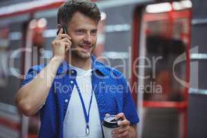 Handsome holding disposable cup while talking on mobile phone