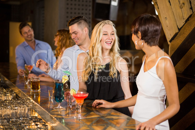 Group of friends interacting with each other at bar counter while having cocktail