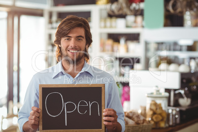 Portrait of waiter showing chalkboard with open sign