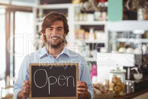 Portrait of waiter showing chalkboard with open sign