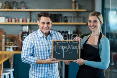 Waitress and man standing with open sign on slate in cafe