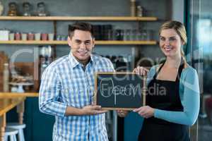 Waitress and man standing with open sign on slate in cafe