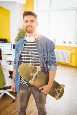 Portrait of handsome executive with skateboard at creative office