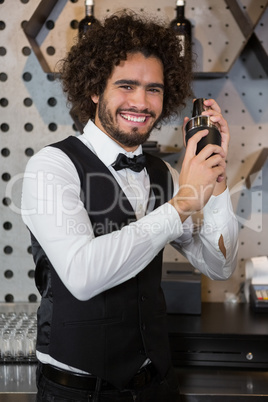 Happy waiter shaking drink in cocktail shaker in a bar