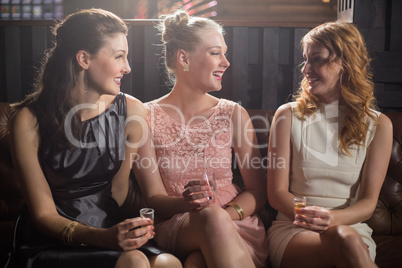 Three female friends interacting with each other while having tequila in bar