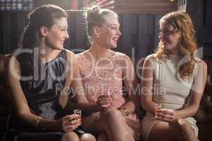 Three female friends interacting with each other while having tequila in bar