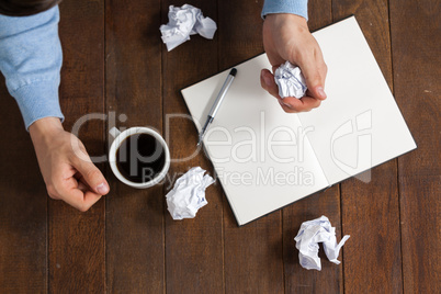 Man crumpling paper while having cup of coffee