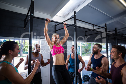 Smiling friends cheering woman doing chin-ups in gym