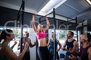 Smiling friends cheering woman doing chin-ups in gym