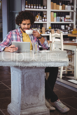 Man having coffee while looking at digital tablet