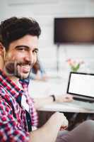 Portrait of confident executive sitting with laptop at creative office