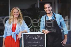 Waiter and woman standing with menu board outside the cafe