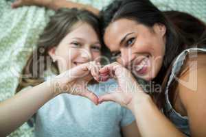 Mother and daughter making heart shape from hand while lying on bed