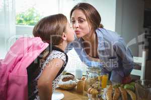 Mother and daughter kissing each other while having breakfast