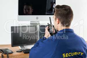 Security officer talking on walkie-talkie while looking at computer monitors