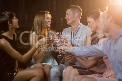 Group of smiling friends sitting on sofa and toasting a glasses of champagne